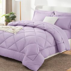 a bed with purple comforter and pillows in a room