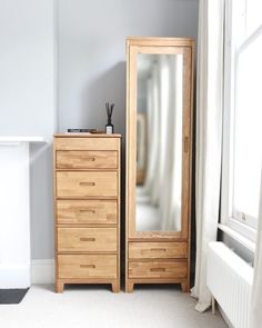 a wooden dresser sitting next to a mirror in a room with white walls and windows