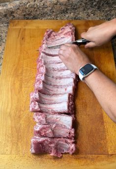 a person cutting up meat on top of a wooden cutting board next to an apple watch