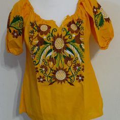 a yellow blouse with flowers and pineapples on the chest, is hanging on a white wall