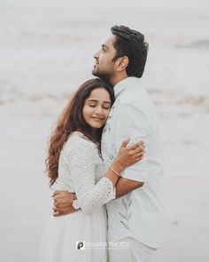 a man and woman hugging on the beach in front of the ocean during their engagement photo session