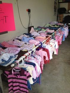 several shirts are lined up on clothes racks in a room with a pink sign hanging from the wall