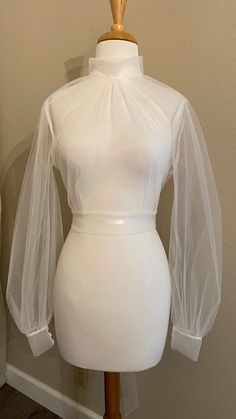 "Tulle wedding dress topper Mock turtle neckline with covered button closure at back neck Open 'V' back with long ties at back waist Bishop sleeves with cuffs/covered buttons **Made to order** Available up to 40\" bust Choose off-white or pale ivory - or ask for a specific color! Rush orders available - please ask about pricing & timing!" White Fitted Blouse With Sheer Sleeves, High Neck Fitted Party Blouse, Fitted High Neck Blouse For Party, High Neck Fitted Blouse For Party, Elegant Tops With Sheer Sleeves And High Neck, Fitted Wedding Top With Sheer Bodice, Elegant Stretch Tops For Wedding, Sheer Long Sleeve Blouse For Wedding, Elegant Fitted Blouse With Mesh Sleeves