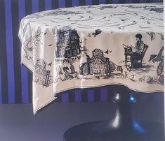 a table cloth with black and white images on it, sitting in front of a blue striped wall