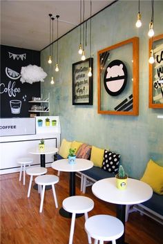 the interior of a coffee shop with white tables and yellow pillows on the chairs,