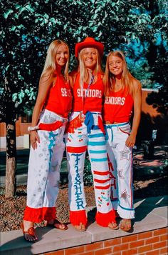 three girls in red shirts and white pants standing next to each other on a brick wall