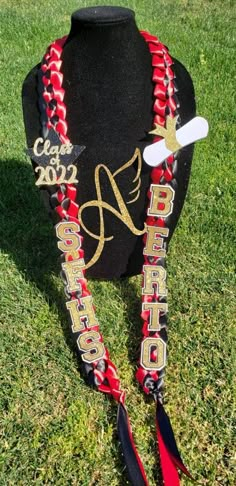 a red and black graduation necklace with gold lettering on it, sitting in the grass