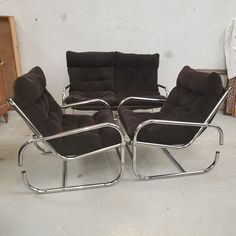 two chairs and a reclining chair are in a room with white walls, one has black cushions on it