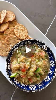 a blue and white bowl filled with food next to crackers on top of a table