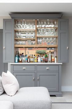 a kitchen with grey cupboards and shelves filled with bottles, glasses, and drinks