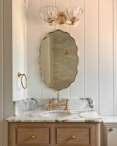 a bathroom vanity with marble counter top and gold faucet light fixture above it