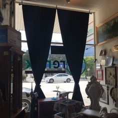 the inside of a store with black curtains and furniture on display in front of an open window