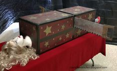 a small dog laying on top of a red blanket next to a chest and box