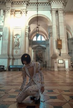 a woman kneeling down in front of a building with an ornate ceiling and arches on the walls