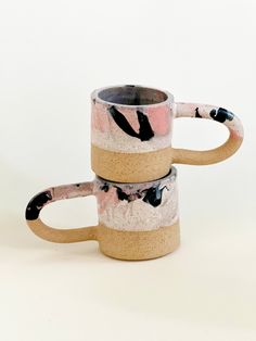 two coffee mugs sitting next to each other on a white surface with black and pink designs