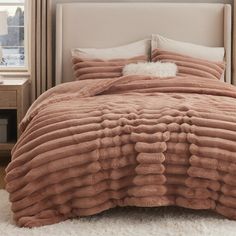 a bedroom with a bed covered in a pink comforter and two pillows on top of it