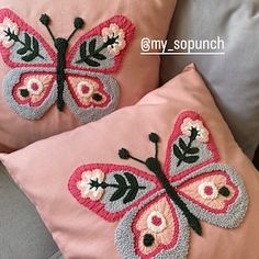 two pink pillows with butterfly appliques on them sitting on a gray couch