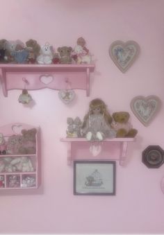 there are many stuffed animals on the shelfs in this pink room with pictures and frames