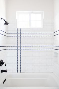 a bath tub sitting under a window next to a white tiled wall and floor in a bathroom