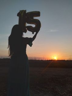 a woman in a long dress holding up a number 50 balloon at the sun set