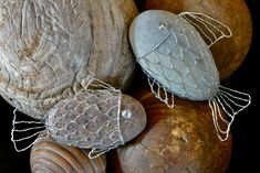 two metal fish sculptures sitting on top of some large rocks with wire wrapped around them