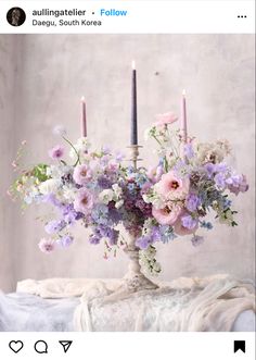 a vase filled with purple and white flowers on top of a table next to two candles