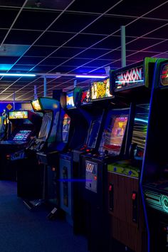 several video game machines lined up in a room with neon lights on the ceiling and blue carpeting