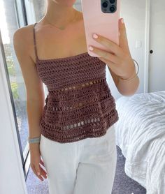 a woman taking a selfie with her cell phone in front of her, wearing white pants and a crocheted top