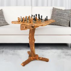 a wooden table with chess pieces on it in front of a white couch and pillows