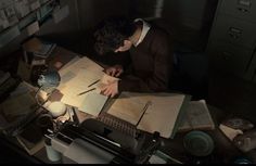 a man sitting at a desk in front of an open book and writing on it