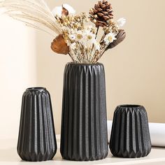 three black vases with flowers in them sitting on a table next to each other