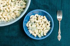 a bowl of macaroni and cheese next to a fork on a blue place mat