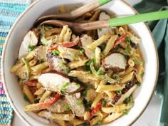 a white bowl filled with pasta and meat on top of a blue table cloth next to green chopsticks