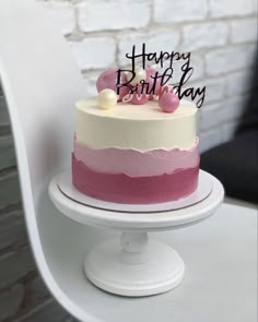 a birthday cake with pink and white frosting on a pedestal in front of a brick wall