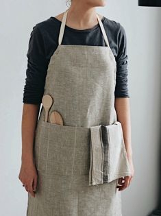 a woman wearing an apron with a wooden spoon in her pocket, standing next to a window