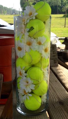 a vase filled with tennis balls and daisies