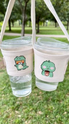 two plastic cups hanging from a tree with cartoon images on the lids and bottom one is filled with water