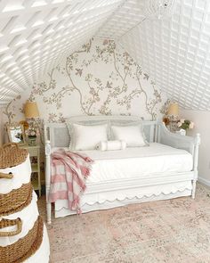 a white bed sitting in a bedroom next to a wall covered in floral wallpaper