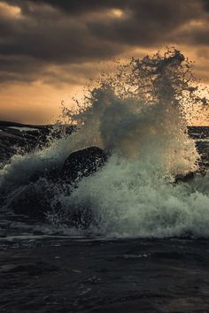 an ocean wave hitting on rocks in front of a cloudy sky