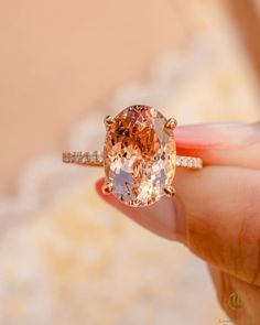 a close up of a person's hand holding a ring with an orange diamond