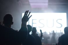 silhouettes of people raising their hands in front of a large screen with the word jesus on it