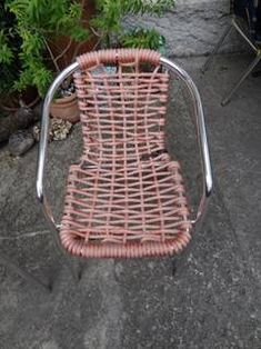 a pink wicker chair sitting on top of a stone floor next to a potted plant