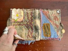 a hand is holding a piece of fabric on top of a wooden table with a flower