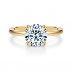 a yellow gold engagement ring with a round cut diamond in the center, on a white background