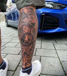 a man with a tiger tattoo on his leg next to a blue sports car in the background