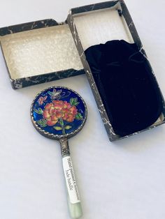 an open box with a mirror inside and a flower design on the lid next to it