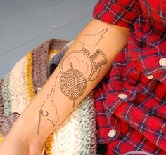 a person with a tattoo on their arm holding a ball of yarn and a sewing needle