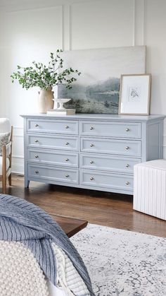 a blue dresser in a bedroom with white walls and wood flooring, along with a painting on the wall