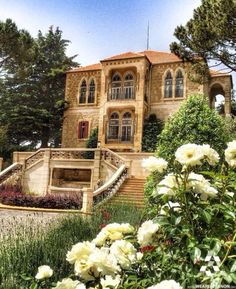 a large house with stairs leading up to it's front door and flowers in the foreground