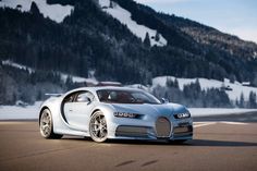 a white bugatti driving down a road next to a snow covered mountain range